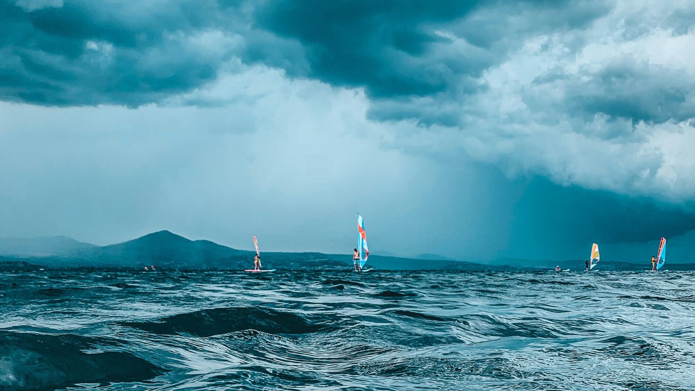 a group of sailboats in the ocean under a cloudy sky