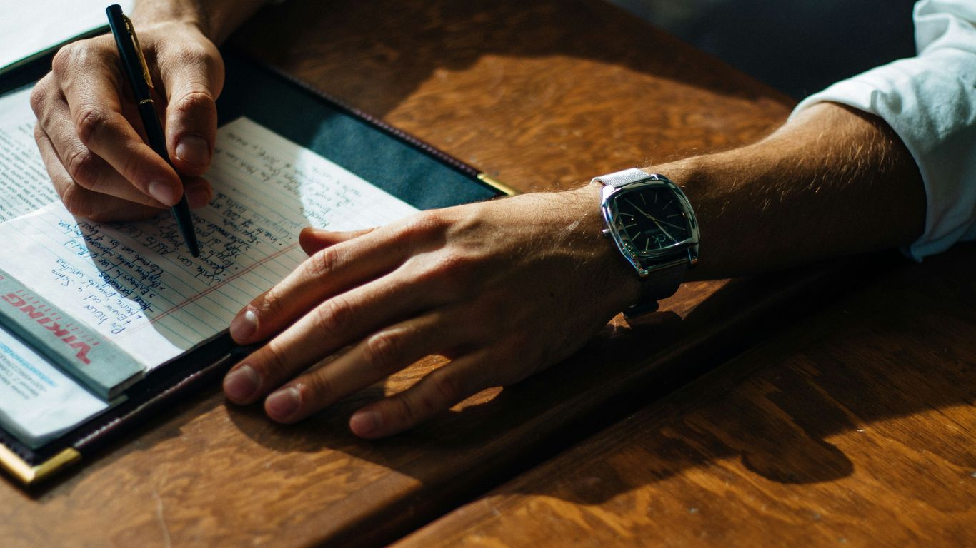 person writing on paper leaning on brown table
