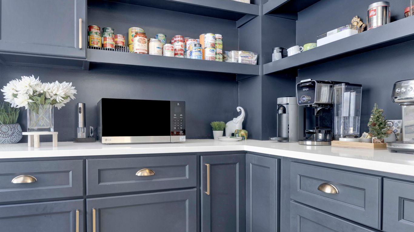 A modern pantry with dark blue cabinets, organized shelves, and a coffee maker.