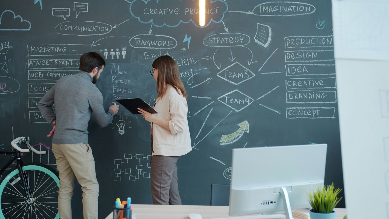 Two people brainstorming on a chalkboard wall.