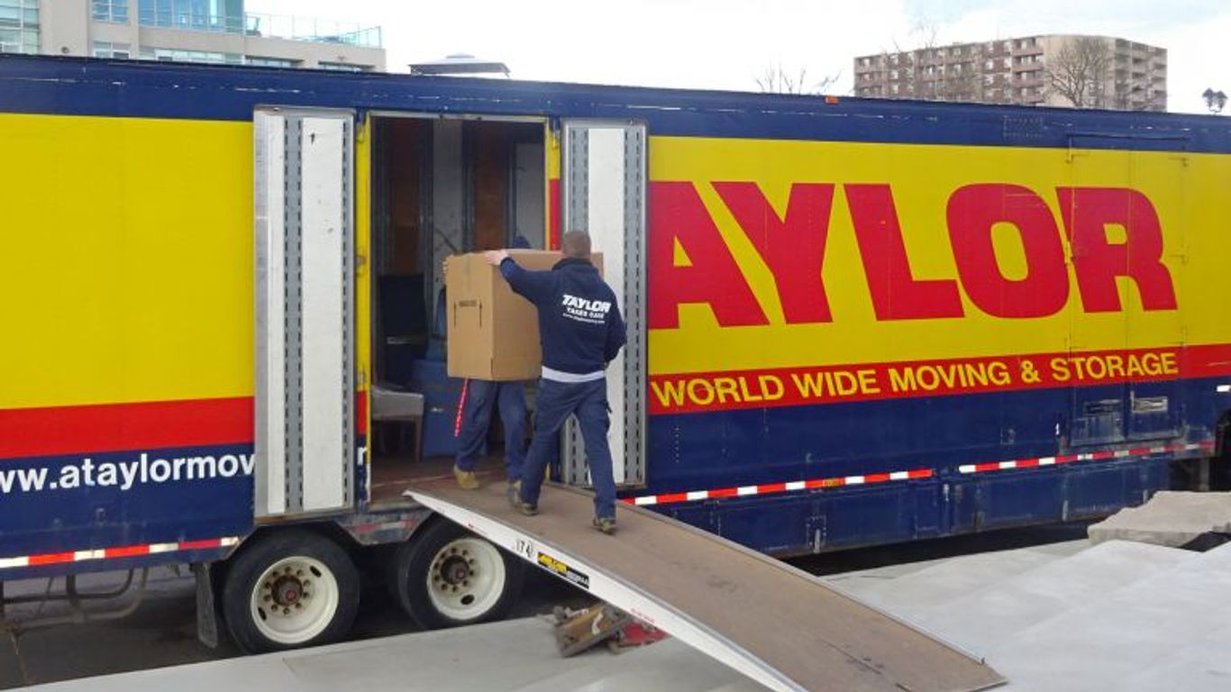 Moving truck with people loading boxes onto a ramp.