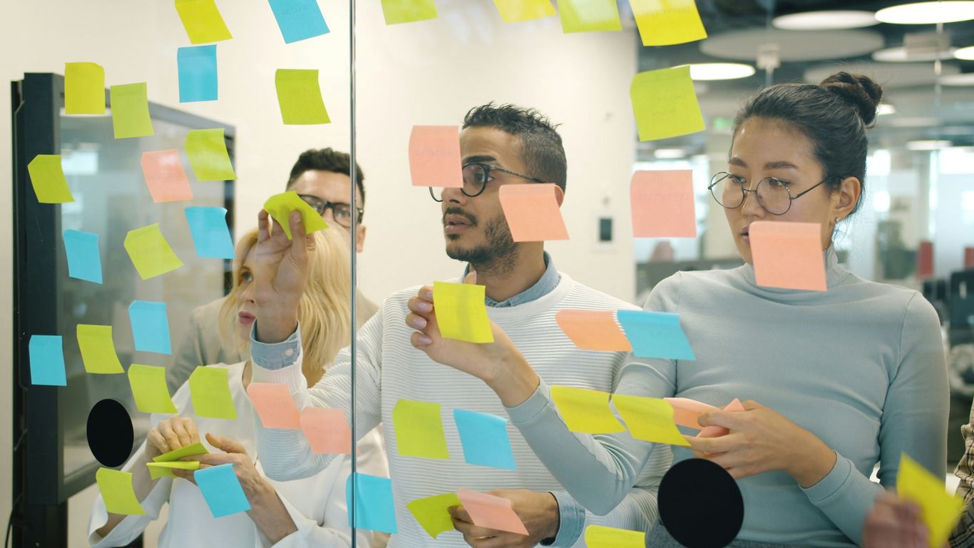 Team brainstorming ideas on a glass wall with sticky notes.