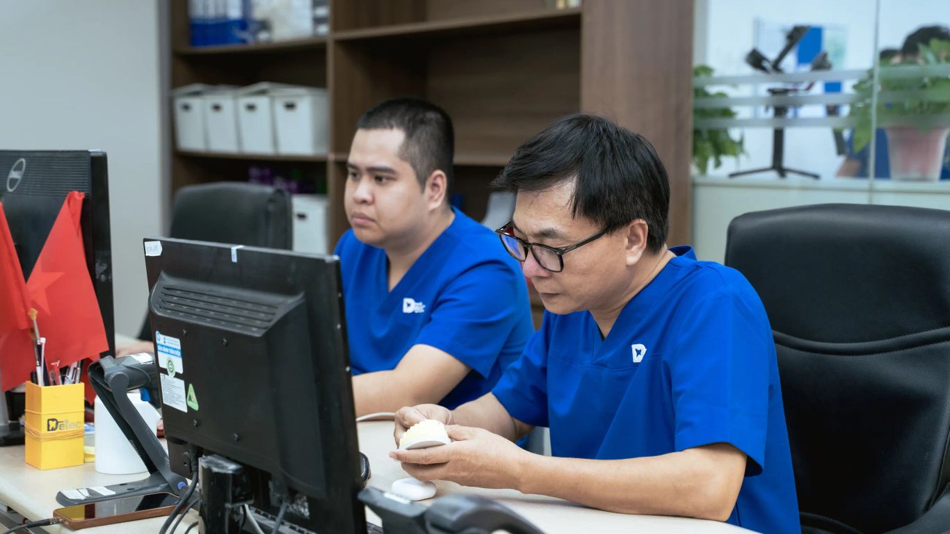 Two people in blue scrubs working at computers with dental models.