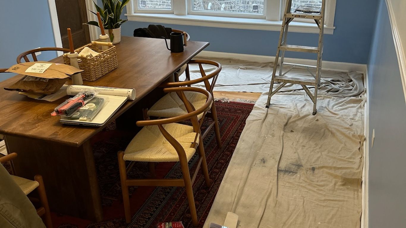 Room being painted with drop cloths, paint, and a ladder.