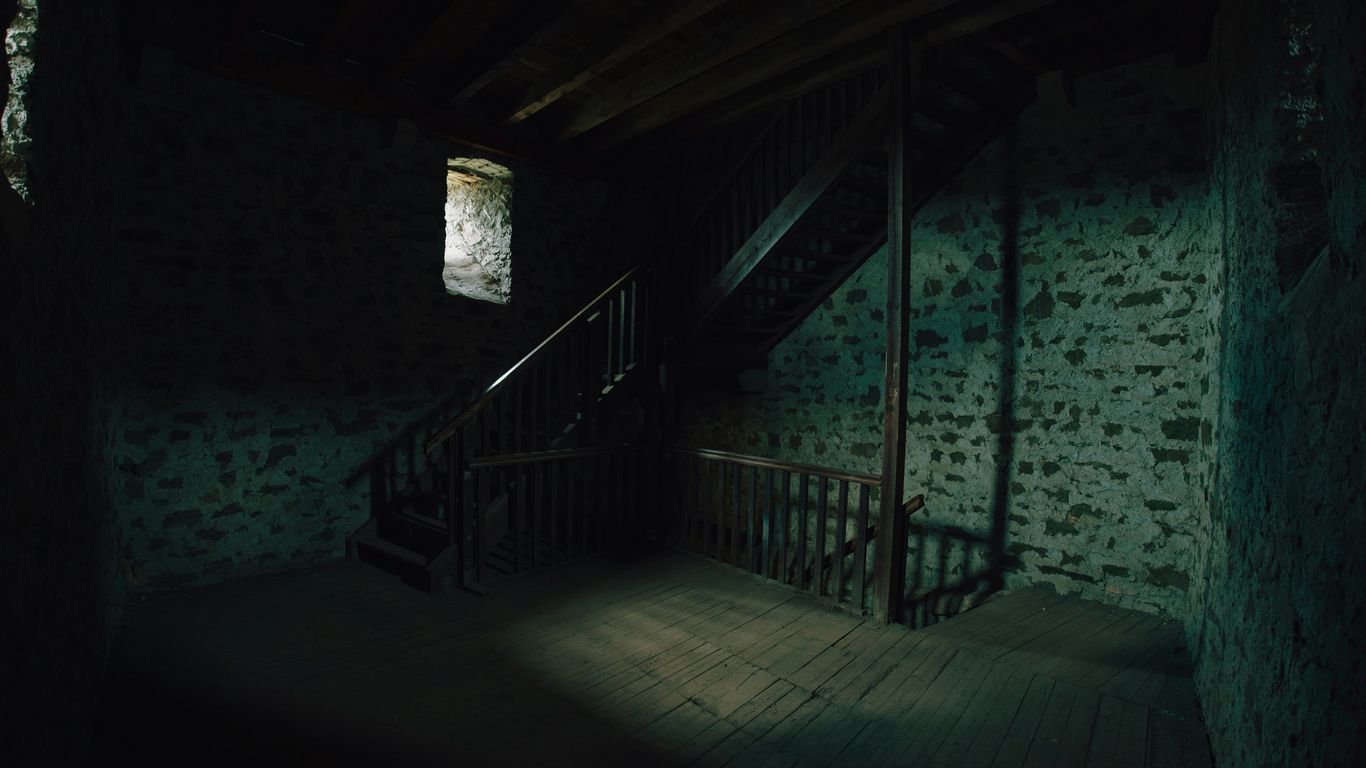 Dark, spooky attic with wooden stairs and window.