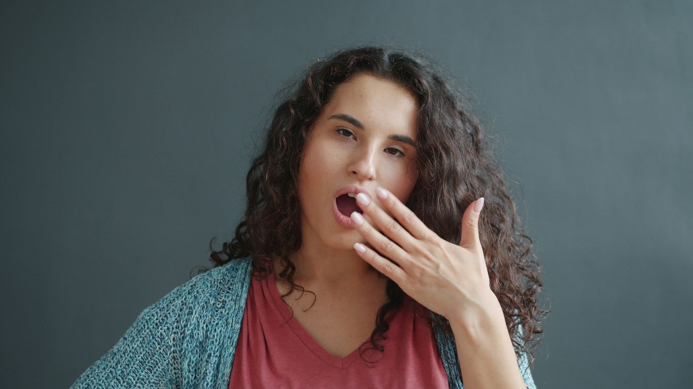 A young woman yawning with her hand over her mouth.