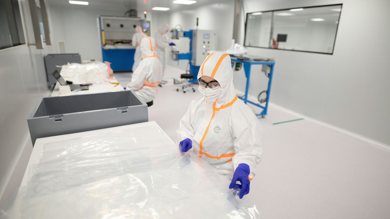 Workers in protective suits inside a cleanroom.