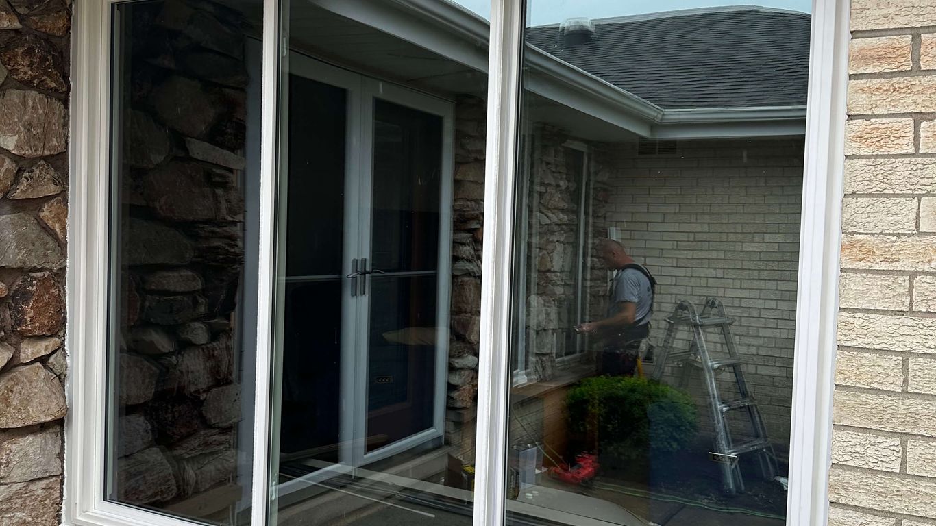 A person works on a window with a ladder and tools.