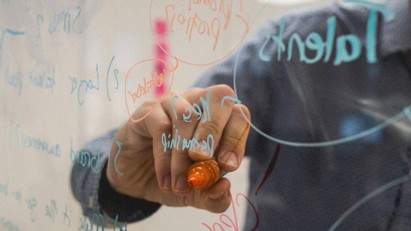 person writing on glass whiteboard with diagrams