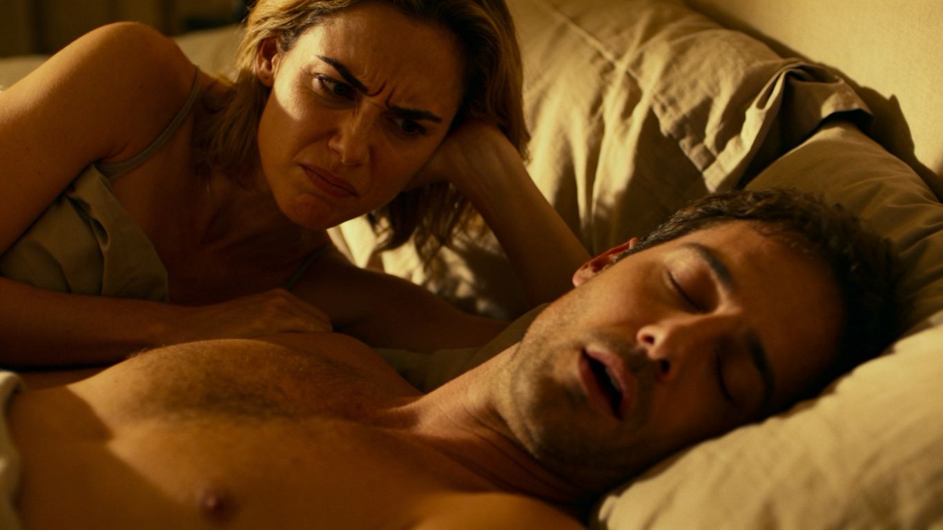 Couple in bed, one partner awake, the other asleep and snoring.