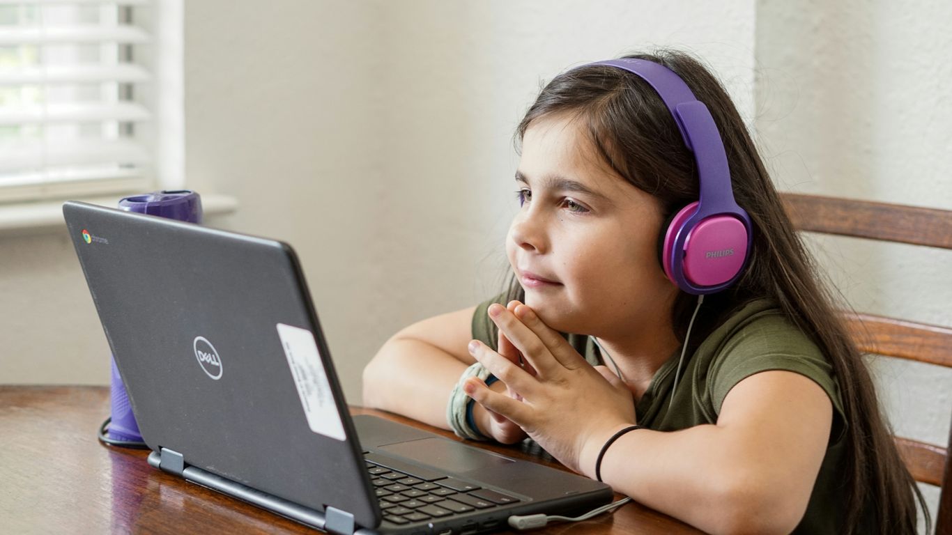 a little girl sitting at a table with a laptop