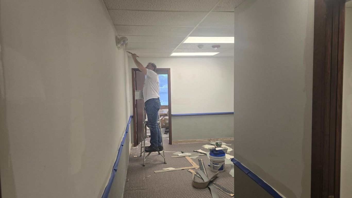 A person is painting a wall in a hallway with blue tape on the walls.