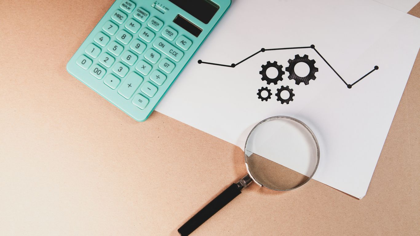 Calculator, magnifying glass, and chart with gears on paper.