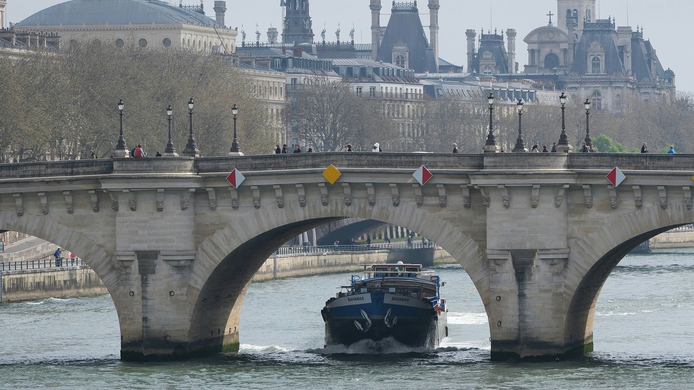 A boat sails under a parisian bridge.