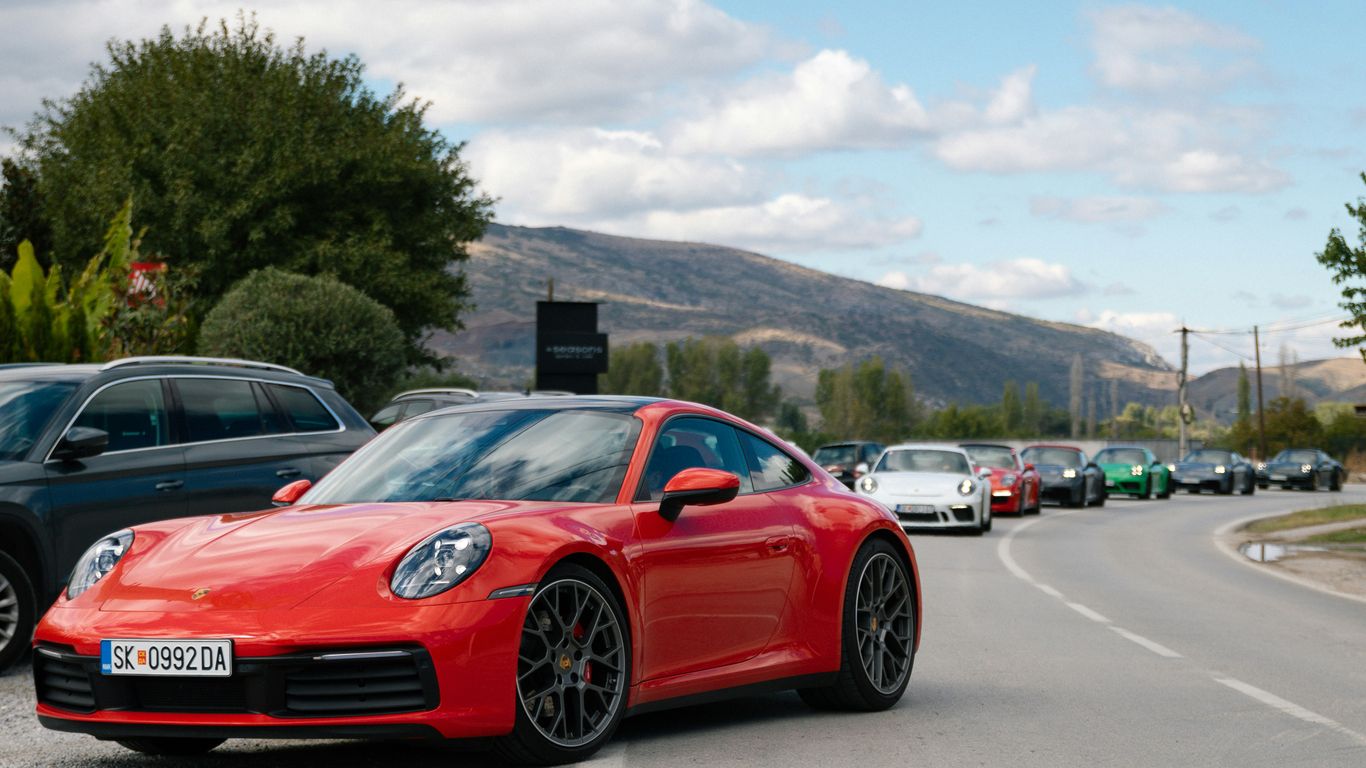 Red porsche leads a line of cars on a road