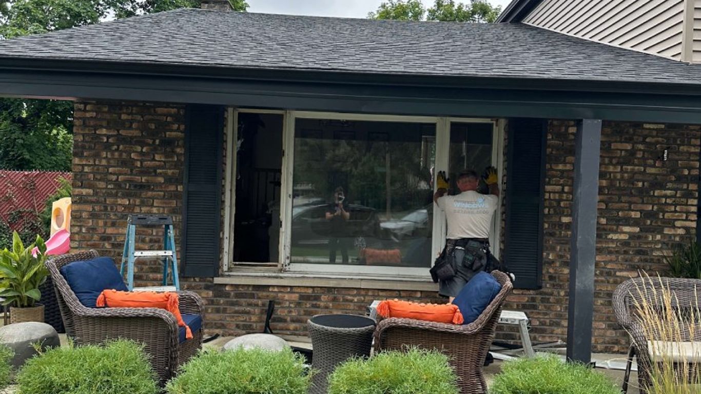 Person installing a window on a brick house with landscaping.