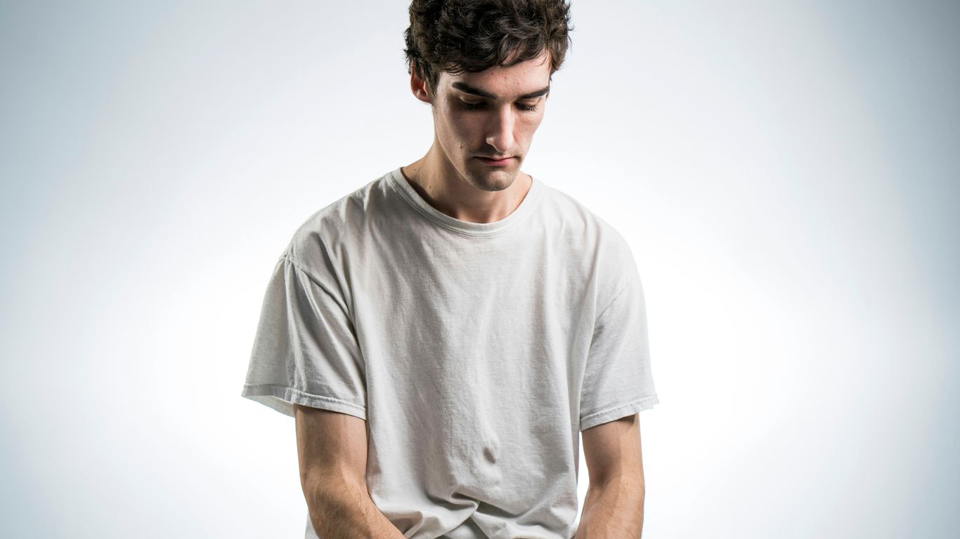 man wearing white crew-neck t-shirt sitting while looking down