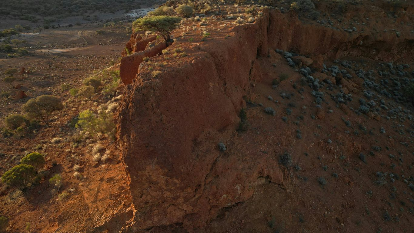 Red rock cliff face with sparse vegetation and dry earth.