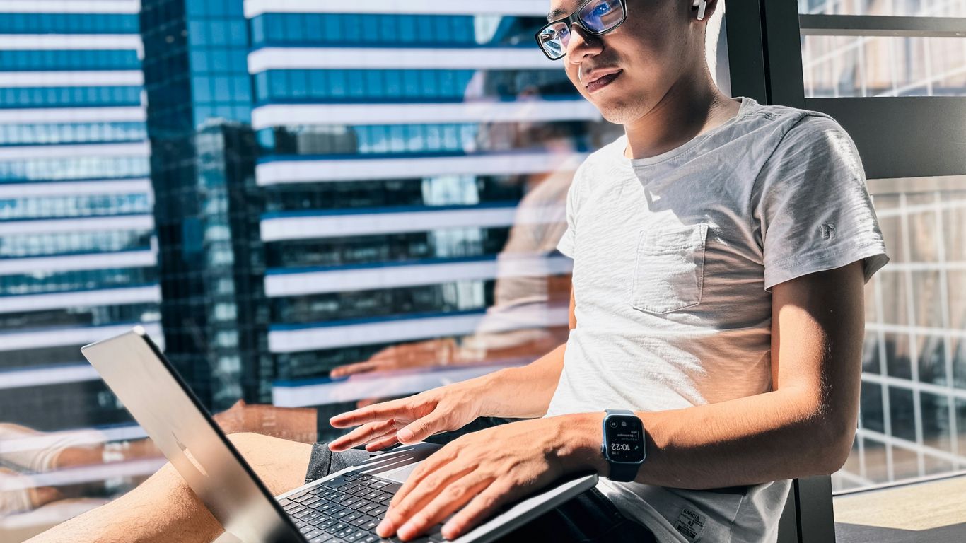 a man sitting in front of a window using a laptop computer