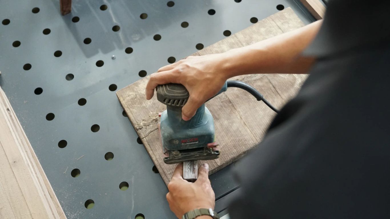 Hands using a sander on a piece of wood.