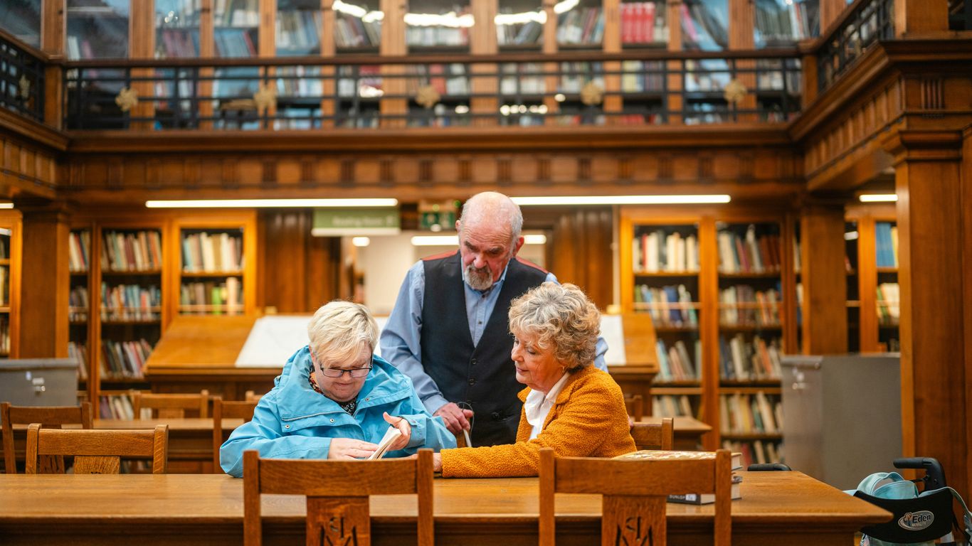 Three people gathered at a wooden table in library.