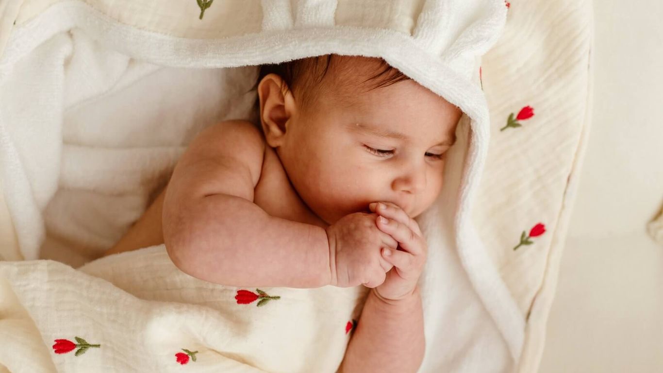 A baby sleeps peacefully wrapped in a floral-patterned blanket with bunny ears.