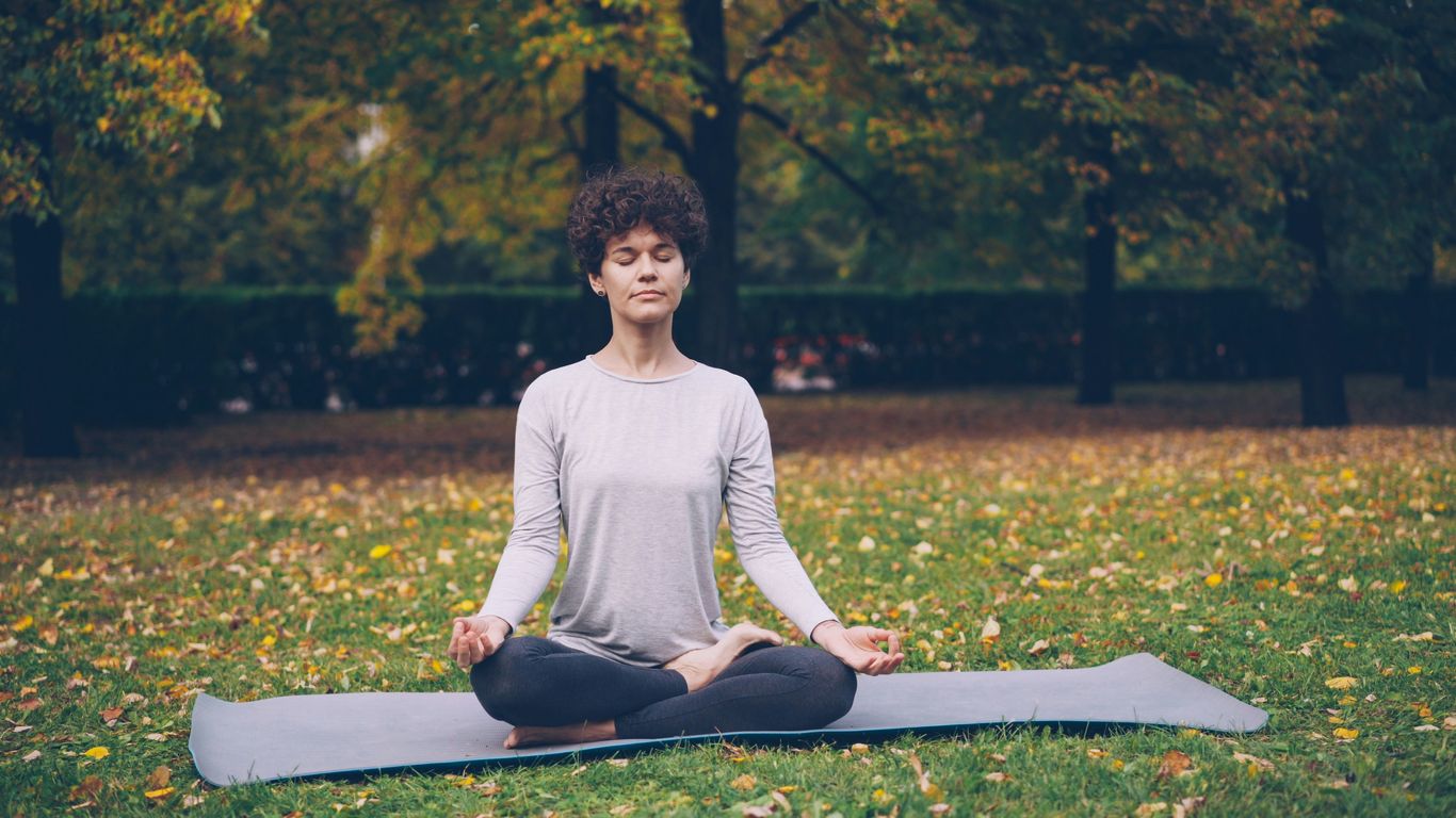 Woman meditating peacefully on a yoga mat outdoors.