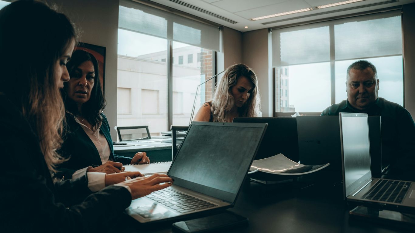 a group of people sitting around a table with laptops