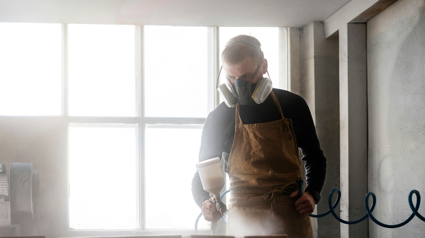 Man wearing respirator and apron working in workshop.
