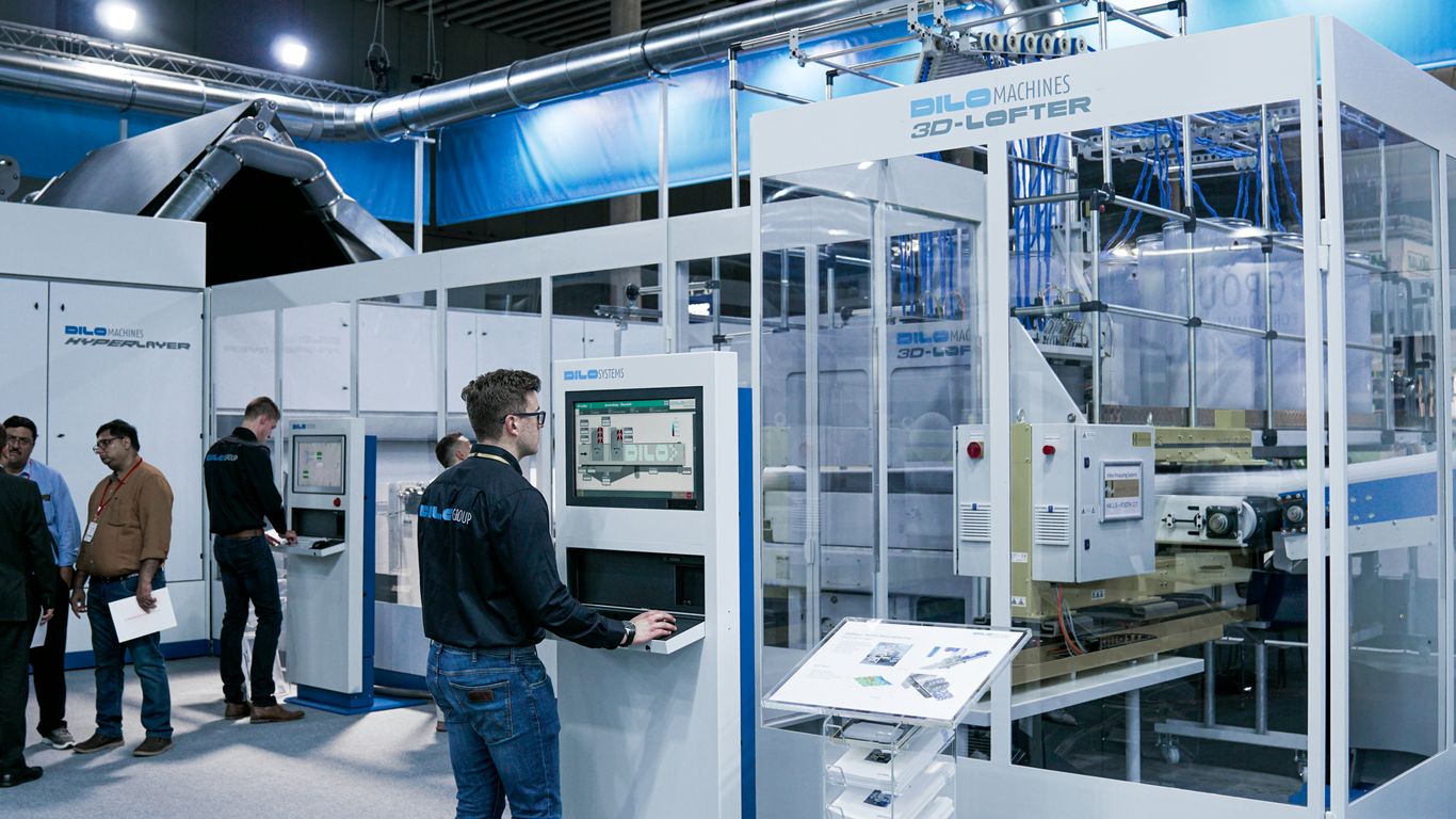 man standing while using computer and another group of men chatting