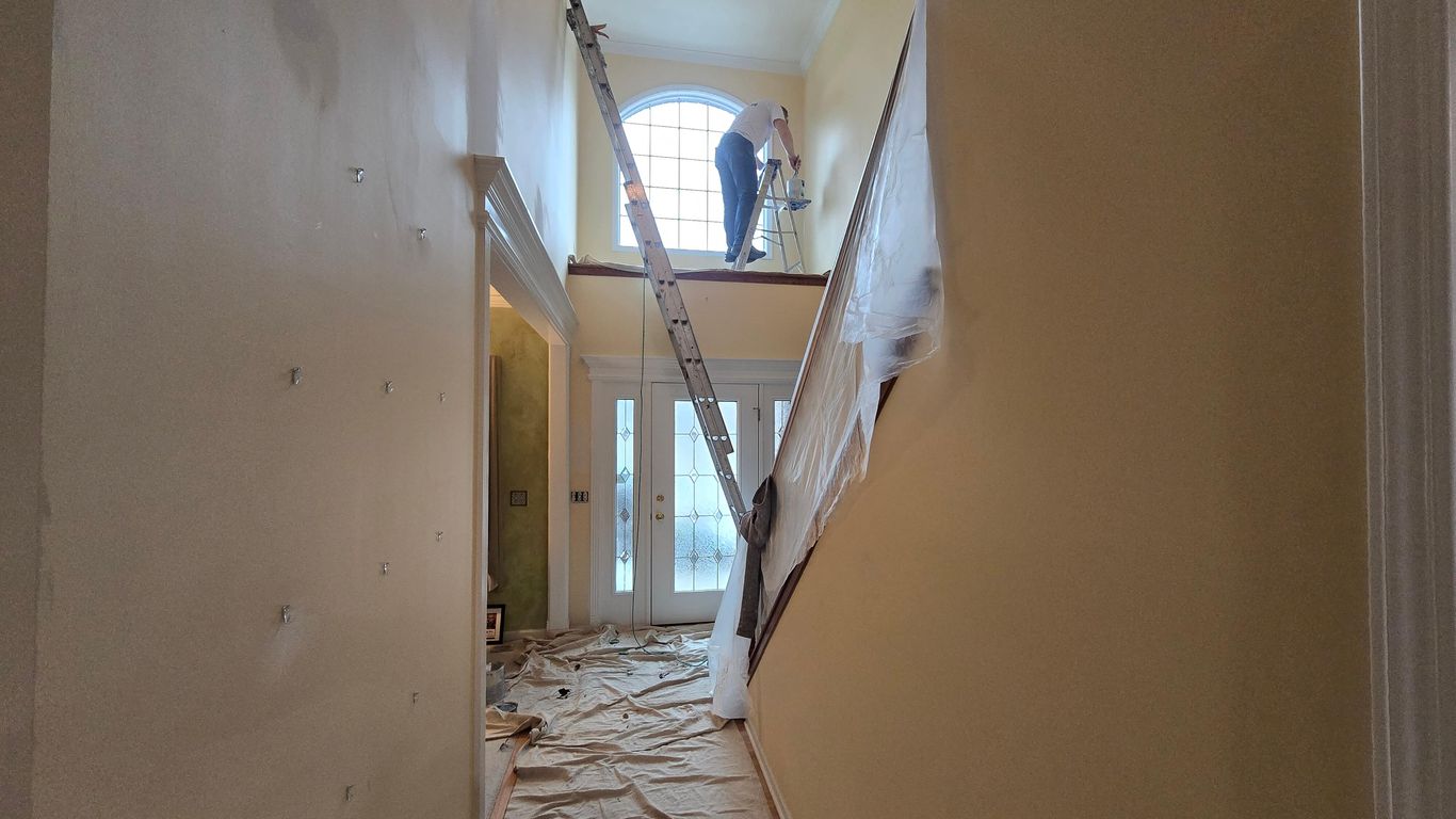 Interior hallway with a person painting on a ladder near a window.