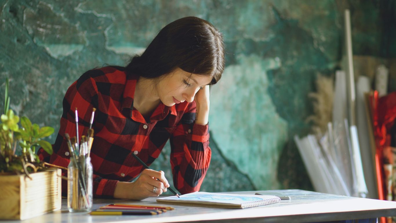 Young woman sketching at a table with art supplies.