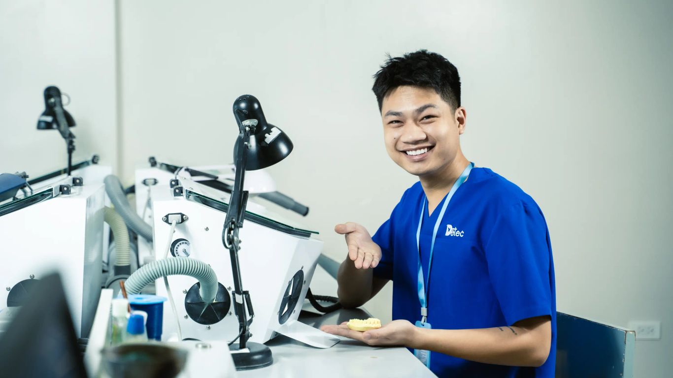 A person in a blue uniform holds a dental model in a lab.