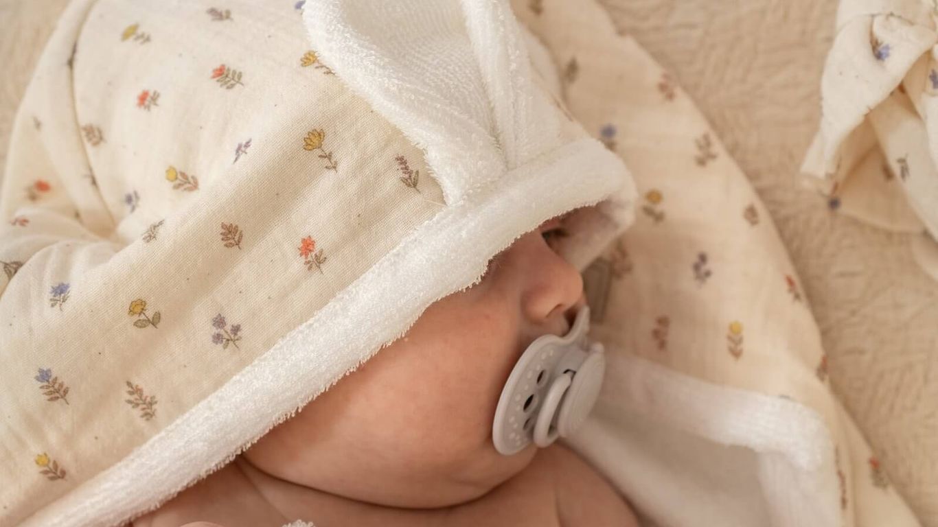A baby wrapped in a floral hooded towel with a pacifier.