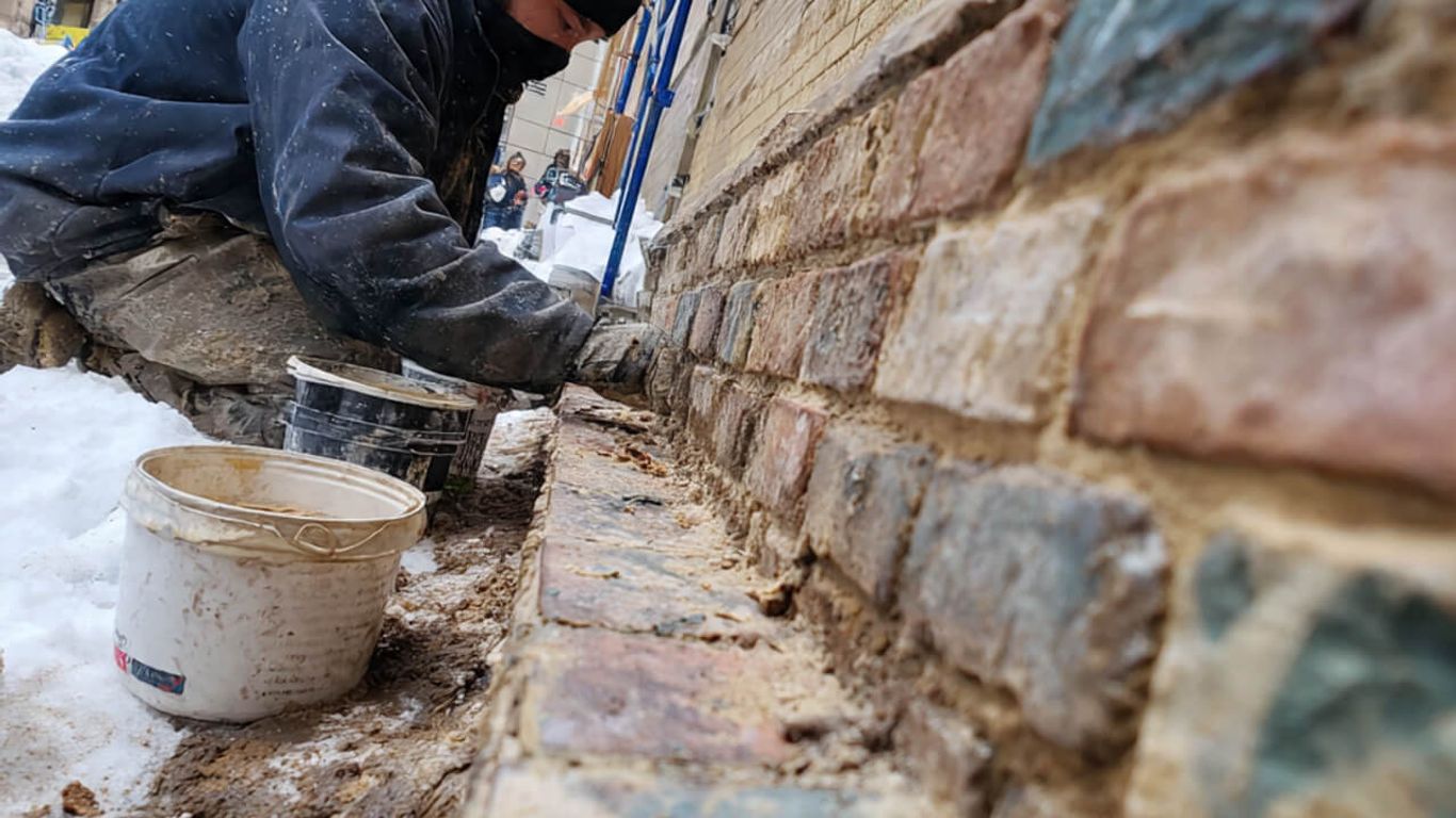 A person works on a brick wall in the snow.