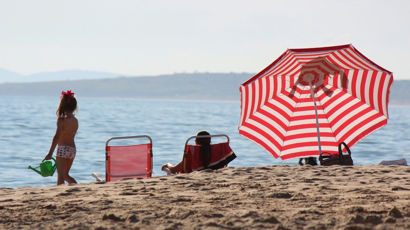 a little girl standing on a beach next to a red and white umbrella
