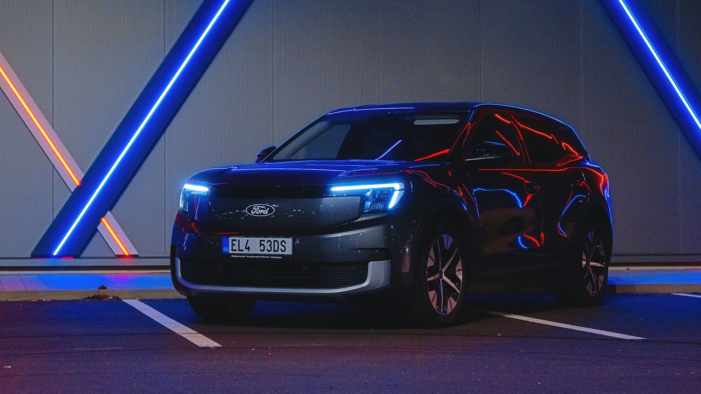 A dark suv parked under neon lights.