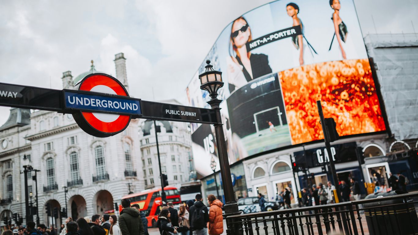 a crowd of people walking on a sidewalk next to a large billboard