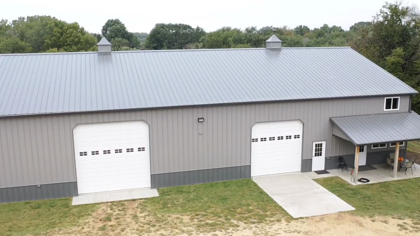 A large gray metal building with two garage doors and a porch.