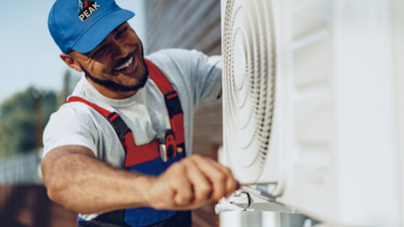 A person in overalls works on an outdoor air conditioning unit.