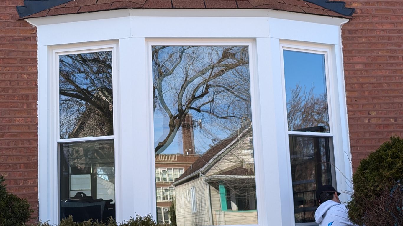A person works on a bay window on a brick house.