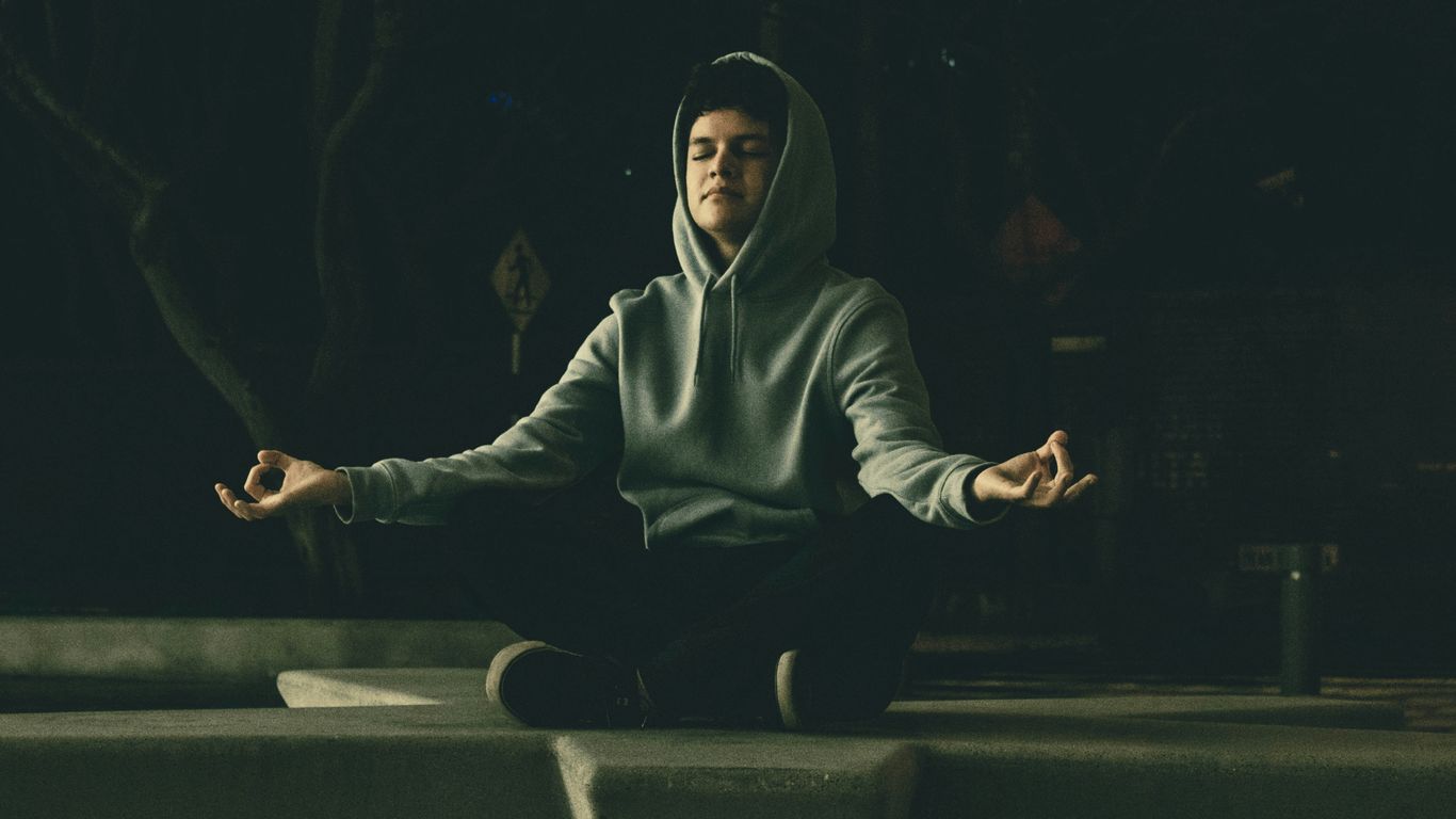 a man in a hoodie meditating in a park at night