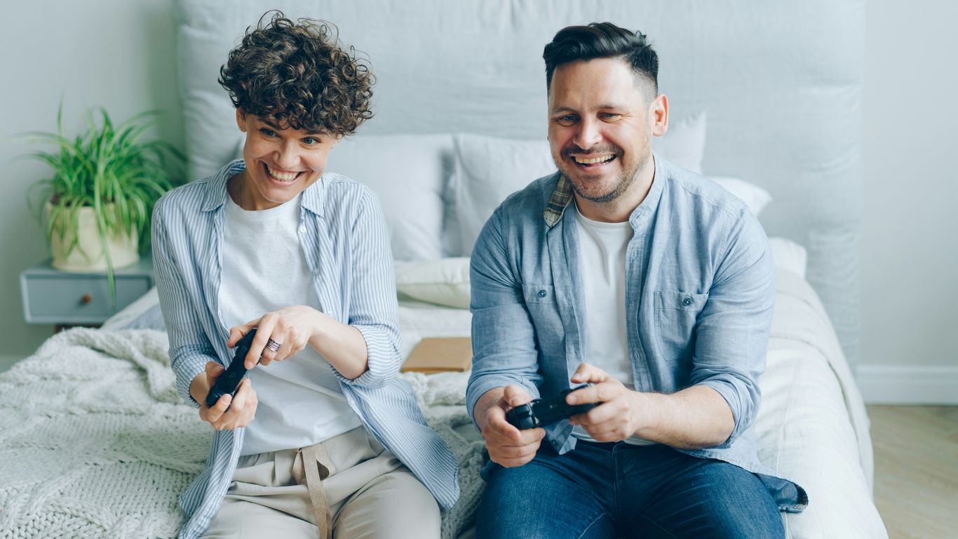 a man and a woman sitting on a bed playing a video game