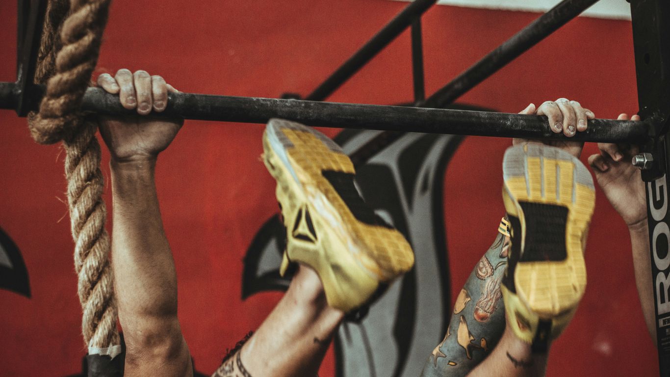person wearing yellow-and-black Reebok low-top athletic shoes hanging on pull-up bar