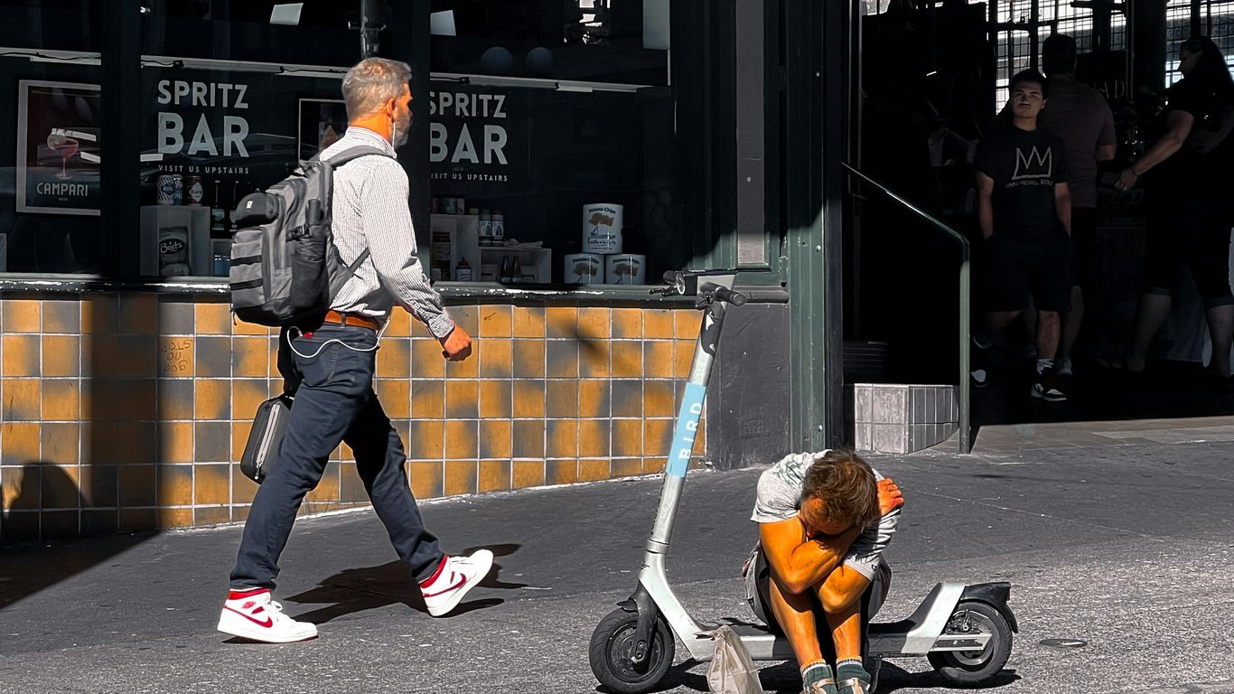 A man walking down a street next to a dog on a scooter