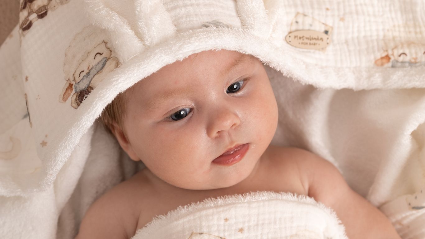 A baby wrapped in a soft blanket with sheep illustrations.
