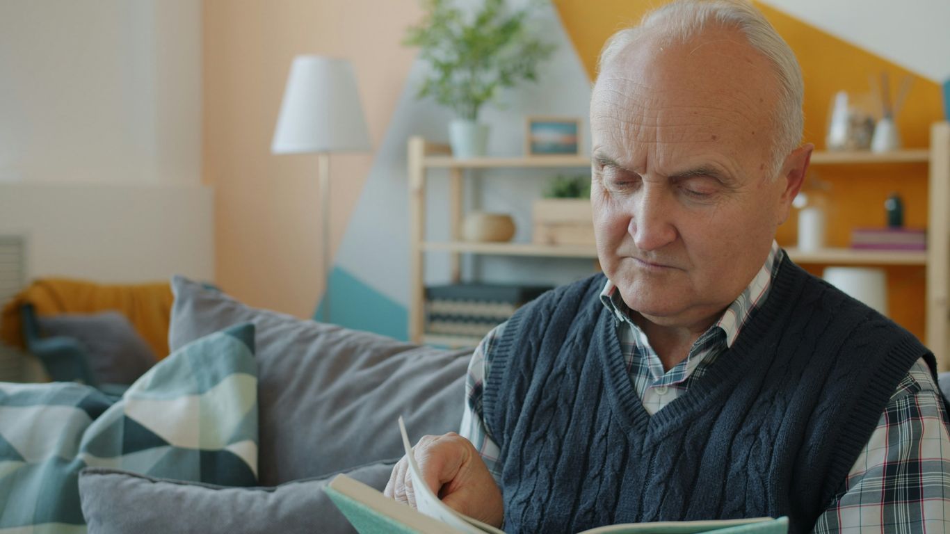 Elderly man reading a book on a couch.