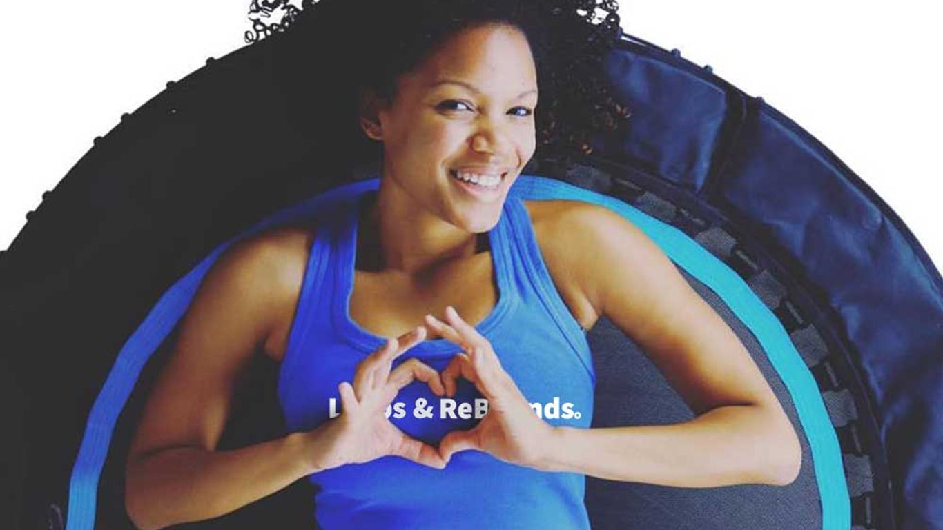 Person lying on trampoline, smiling, making heart shape with hands.