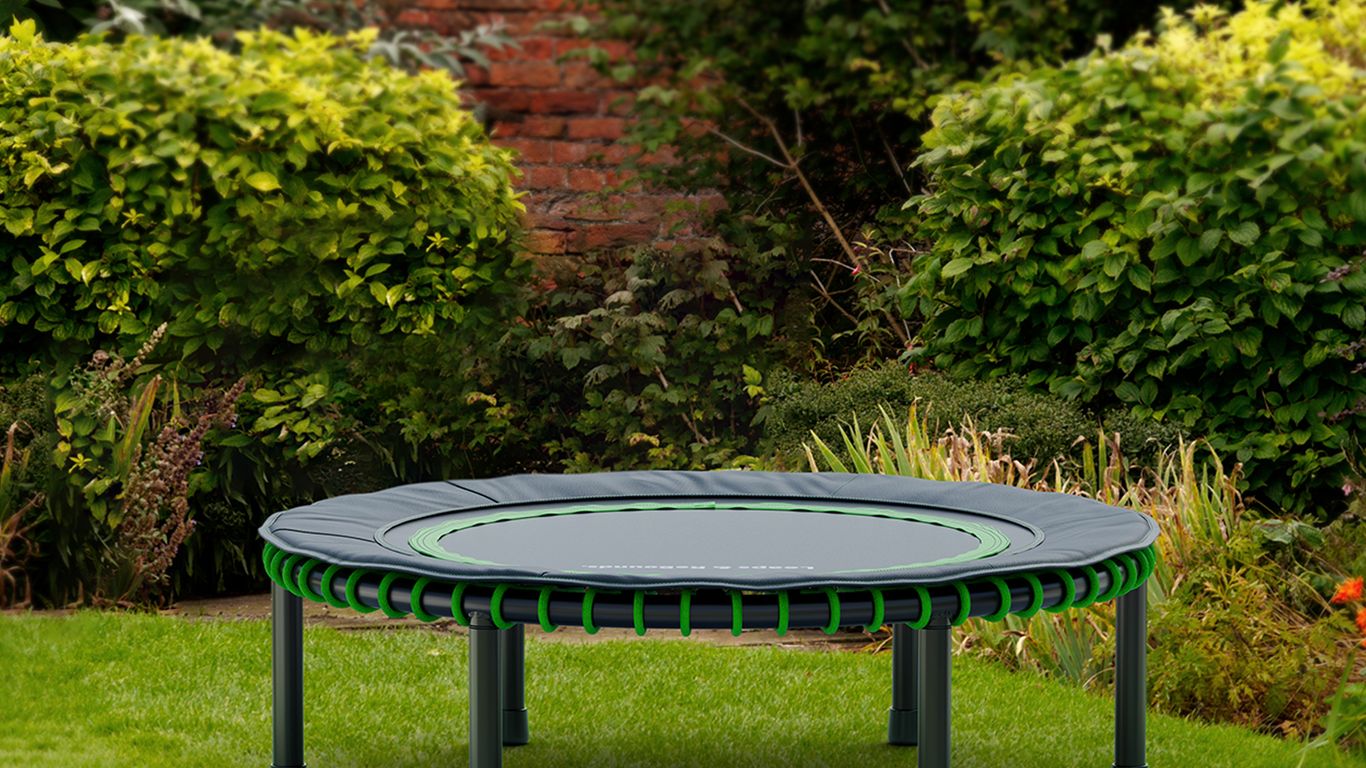 Small trampoline on green grass in a lush garden.