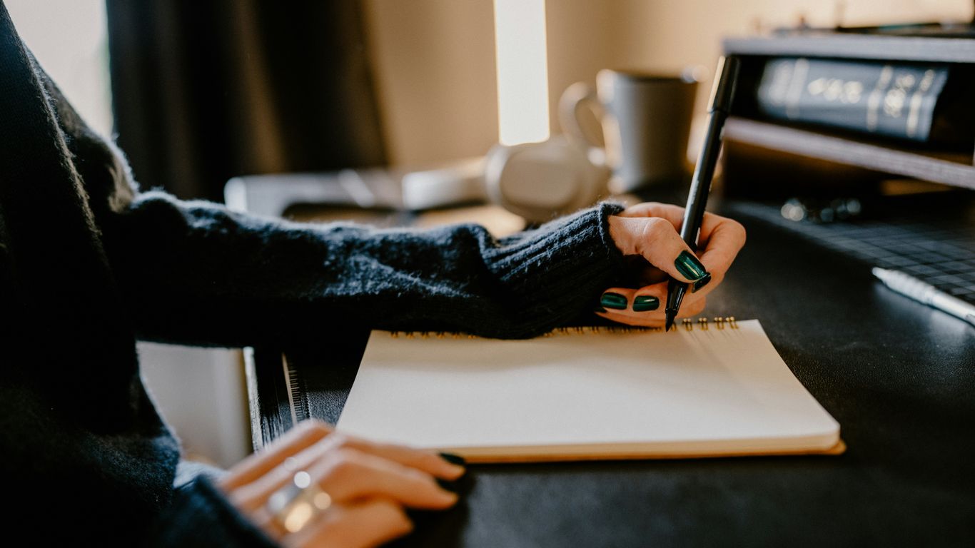 a person holding a pen and writing on a notebook